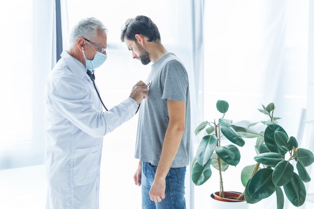 Rancho, California clinic with a senior doctor using a stethoscope to check a male patient’s chest and heart.