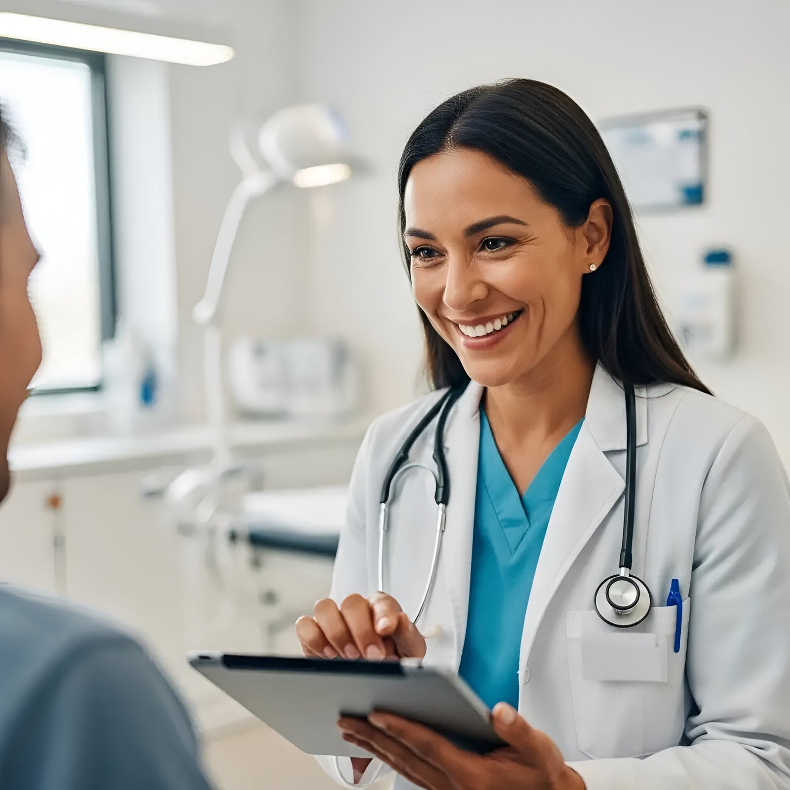 A friendly female healthcare professional in a white lab coat and blue scrubs using a tablet while consulting with a patient in a bright, modern Rancho medical clinic.